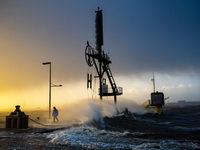Eine Person geht während der Sturmflut bei Sonnenaufgang in Bremerhaven am Wasser spazieren.