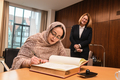 Nadjet Hamdi sitzt am Tisch und trägt sich in das Gästebuch ein. Seitlich versetzt hinter ihr steht Frau Grotheer und sieht ihr dabei zu.